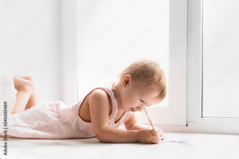 Caucasian baby girl lies and paints on windowsill Caucasian baby girl lies and paints on windowsill