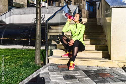 Quenching thirst on a street workout. Fitness woman is drinking water from sports water bottle outdoors.