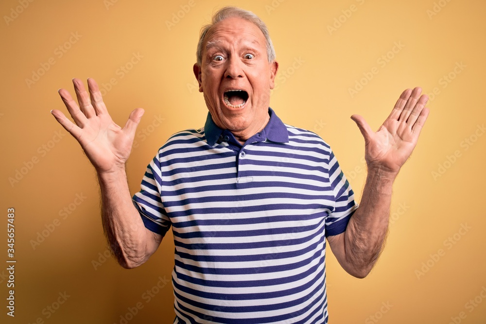 Grey haired senior man wearing casual navy striped t-shirt standing over yellow background celebrating crazy and amazed for success with arms raised and open eyes screaming excited. Winner concept Grey haired senior man wearing casual navy striped t-shirt standing over yellow background celebrating crazy and amazed for success with arms raised and open eyes screaming excited. Winner concept