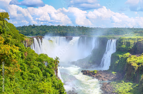 Iguazu waterfalls in Argentina, view from Devil's Mouth. Panoramic view of many majestic powerful water cascades with mist. Panoramic image with reflection of blue sky with clouds.