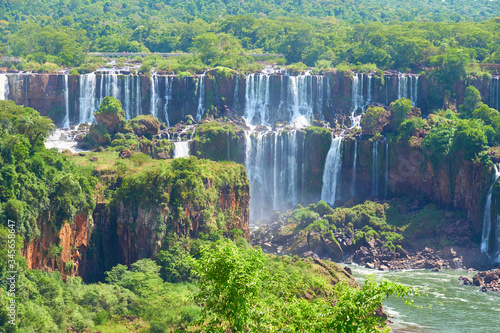 Iguazu waterfalls in Argentina, view from Devil's Mouth, close-up on powerful water streams creating mist over Iguazu river. Sub-tropical trees and shrubs in Iguasu river valley.