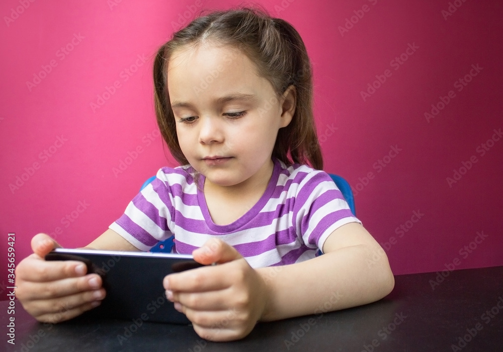 A smiling little girl watching an online video lesson on a smartphone at home, a Cute happy little child calling on a mobile phone with a teacher or tutor, home learning concept A smiling little girl watching an online video lesson on a smartphone at home, a Cute happy little child calling on a mobile phone with a teacher or tutor, home learning concept