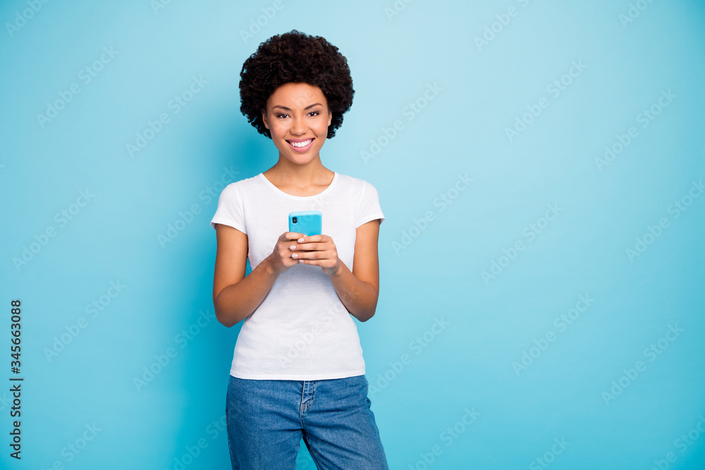 Photo of cheerful beautiful dark skin curly lady holding telephone hands chatting friends sending new pictures wear casual white t-shirt jeans isolated blue color background Photo of cheerful beautiful dark skin curly lady holding telephone hands chatting friends sending new pictures wear casual white t-shirt jeans isolated blue color background