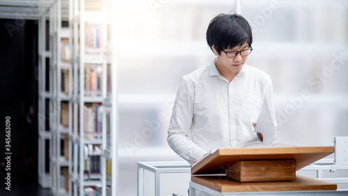 Smart Asian man university student reading recommended book on wooden podium in college library. Education research and Scholarship oppotunity concepts photo