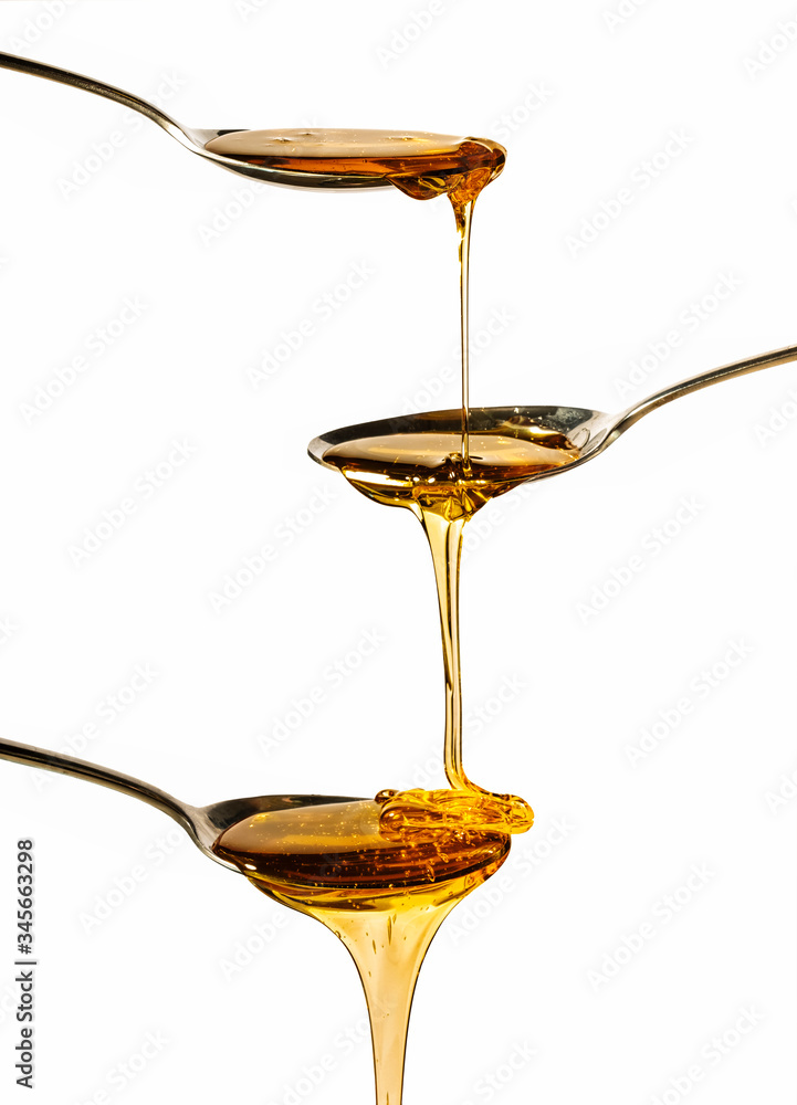 honey falling on metal spoons with a white background honey falling on metal spoons with a white background
