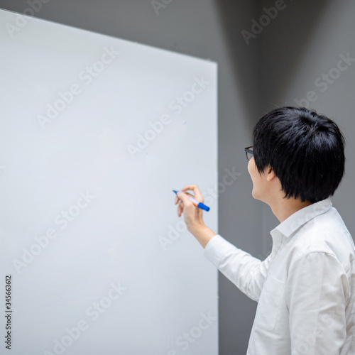 Asian man teacher writing on blank whiteboard teaching lesson in classroom. Male businessman presenting his project to coworkers in office conference room. Education presentation or business meeting