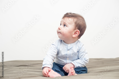 Profile view of a cute baby boy sitting in bed with a peaceful expression.