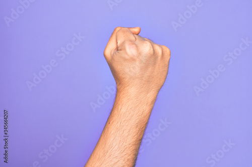 Hand of caucasian young man showing fingers over isolated purple background doing protest and revolution gesture, fist expressing force and power