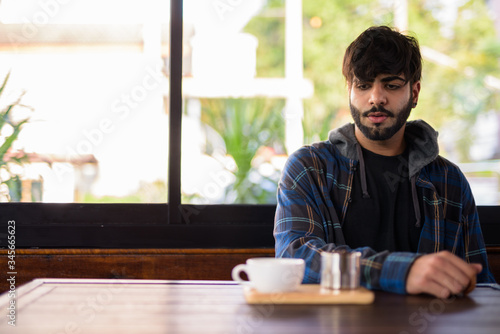 Young handsome bearded Indian hipster man at the coffee shop