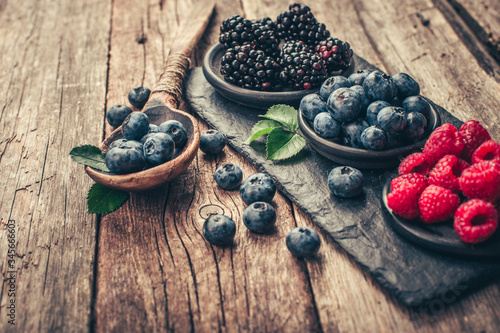 Fresh berries with raspberries, blueberries, blackberries in bowl on a stone stand on wood background.