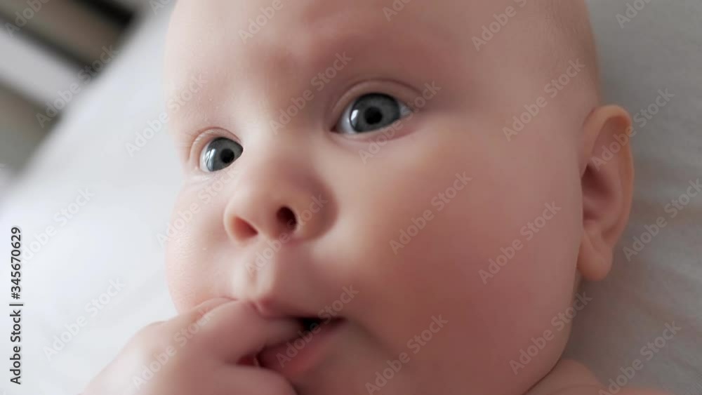 Extreme close up face of cute newborn baby putting finger in mouth lying on cozy white bed Extreme close up face of cute newborn baby putting finger in mouth lying on cozy white bed