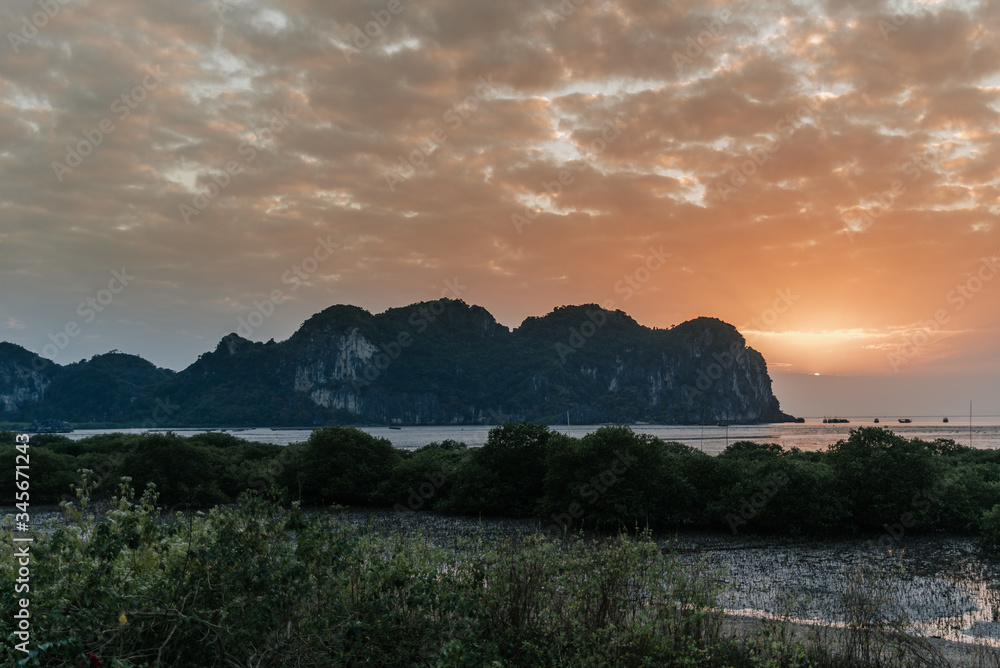 Stunning colorful sunset over the beautiful Karst stone mountain landscape of Ha Long Bay viewed from Cat Ba Island, Vietnam.