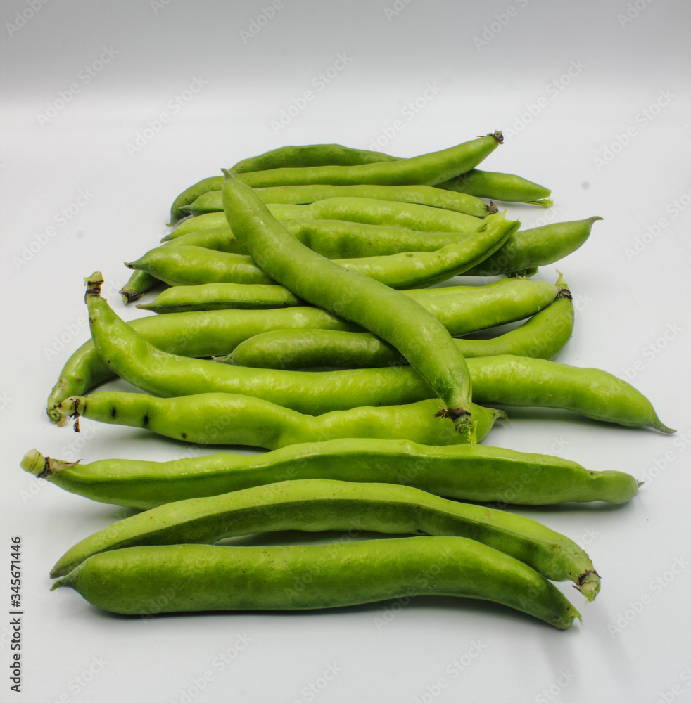 row of fresh green broad beans in their shells isolated on a white background