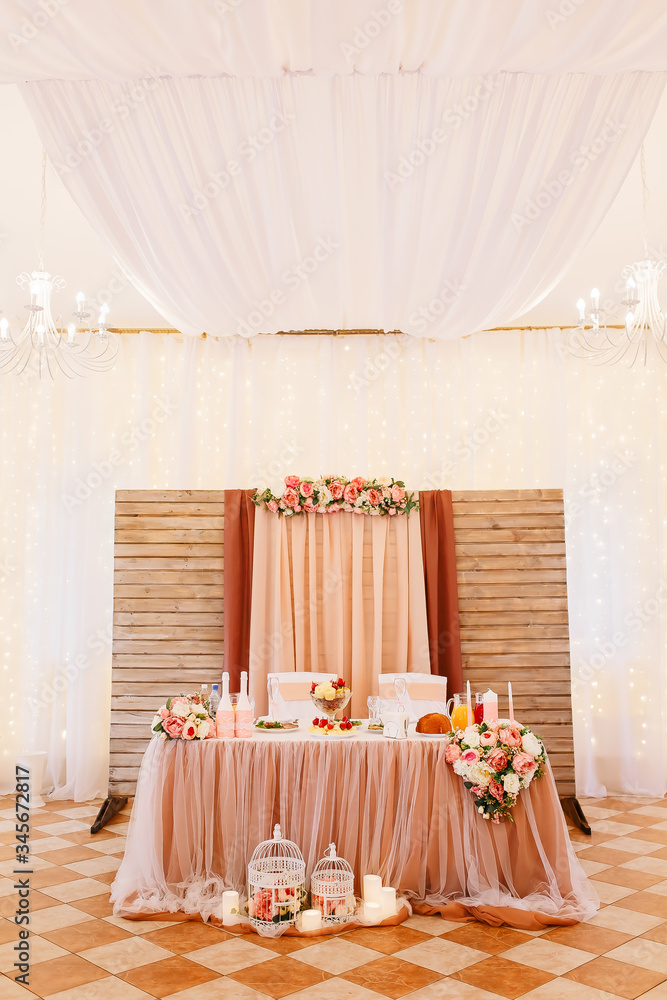 Wedding in the style vintage. Table decoration with cages, candles & candlestick. Elegant dining table in peach-pink color. Indoors wedding reception venue. Table with flowers, bottles, fruits, food.