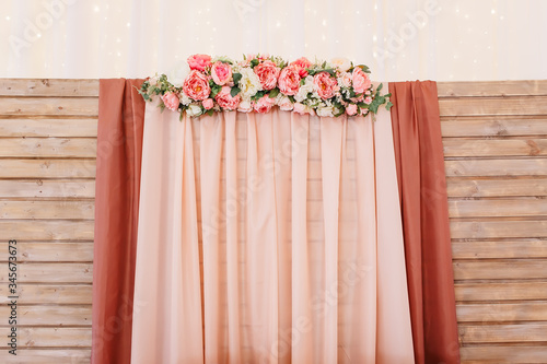 Rustic wedding photo zone. Wedding in the style vintage. Composition with flowers on a wooden stand. A wooden backdrop of chiffon and flowers. Indoors wedding reception venue. Horizontal shot.