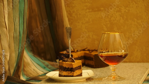 A peace of chocolate cake with a spoon and glass of brandy