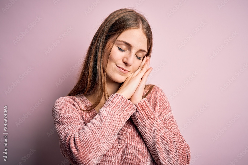 Young beautiful redhead woman wearing casual sweater over isolated pink background sleeping tired dreaming and posing with hands together while smiling with closed eyes. Young beautiful redhead woman wearing casual sweater over isolated pink background sleeping tired dreaming and posing with hands together while smiling with closed eyes.