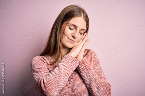Young beautiful redhead woman wearing casual sweater over isolated pink background sleeping tired dreaming and posing with hands together while smiling with closed eyes.