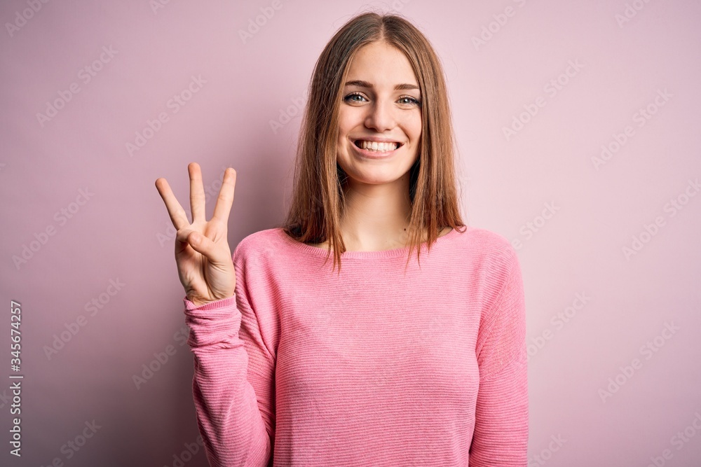 Young beautiful redhead woman wearing casual sweater over isolated pink background showing and pointing up with fingers number three while smiling confident and happy. Young beautiful redhead woman wearing casual sweater over isolated pink background showing and pointing up with fingers number three while smiling confident and happy.