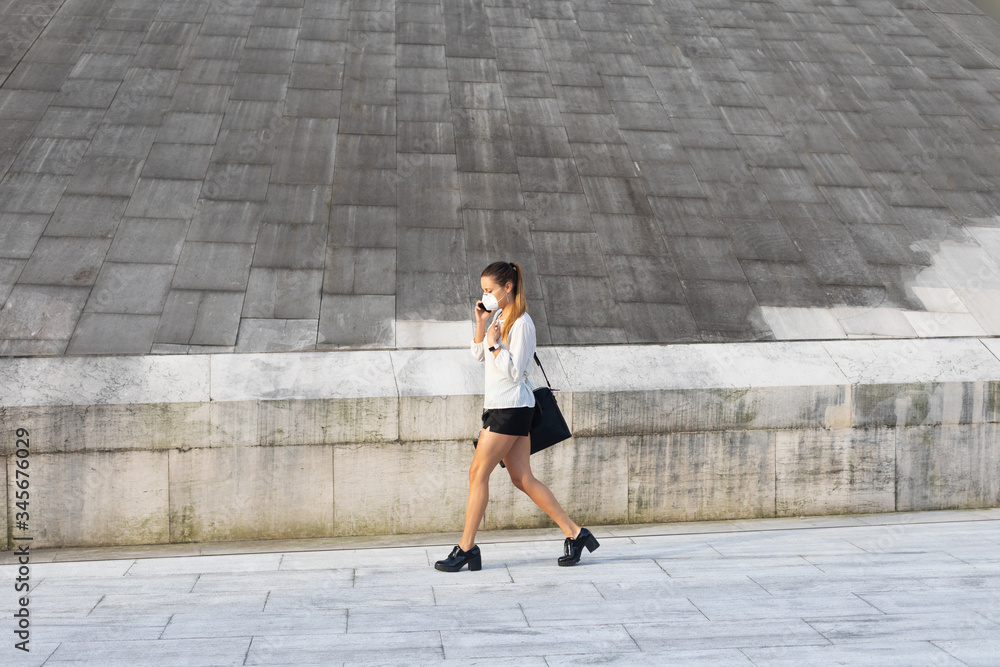 Young busy stylish professional woman with n95 face mask for protecting health against Covid-19 walking and talking on cellphone. Young busy stylish professional woman with n95 face mask for protecting health against Covid-19 walking and talking on cellphone.