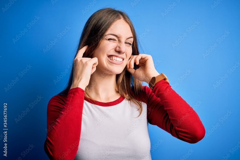 Young beautiful redhead woman wearing casual t-shirt over isolated blue background covering ears with fingers with annoyed expression for the noise of loud music. Deaf concept. Young beautiful redhead woman wearing casual t-shirt over isolated blue background covering ears with fingers with annoyed expression for the noise of loud music. Deaf concept.