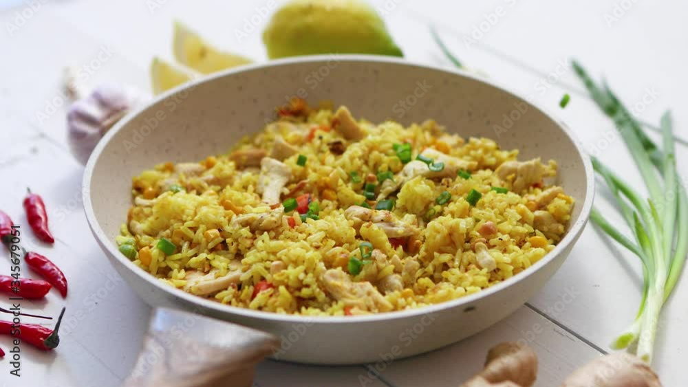 Delicious fried rice with chicken and vegetables served in pan. Placed on white wooden table Delicious fried rice with chicken and vegetables served in pan. Placed on white wooden table