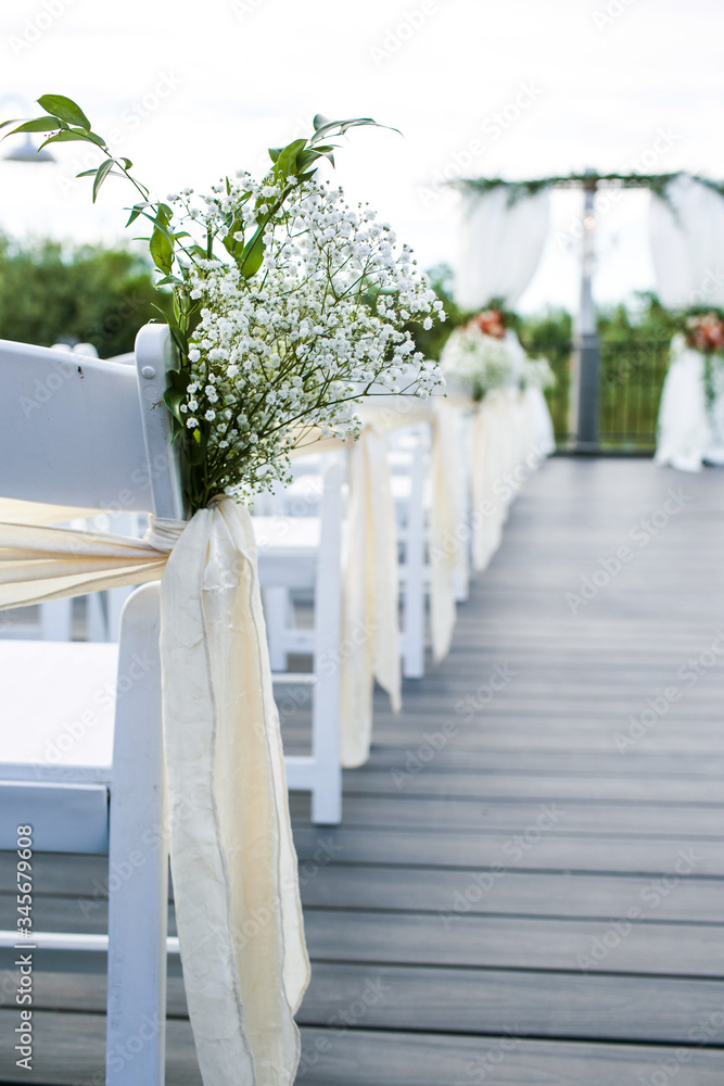 close up of white babies breath flowers tied to white wooden chair and wedding ceremony aisle in the background