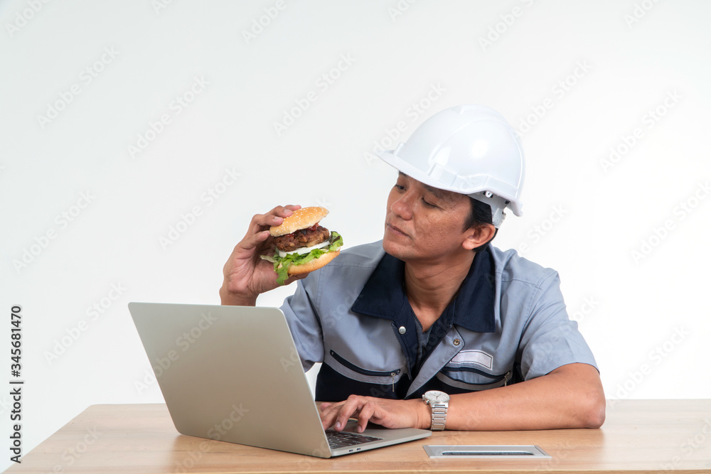Asian man worker smiling and holding a hamburger in the living room While working from home, hem very happy and enjoy to eat fast food. Concept of binge eating disorder (BED). Asian man worker smiling and holding a hamburger in the living room While working from home, hem very happy and enjoy to eat fast food. Concept of binge eating disorder (BED).