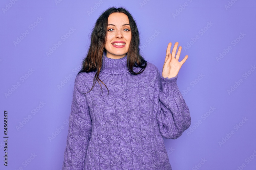 Young beautiful woman wearing casual turtleneck sweater standing over purple background Waiving saying hello happy and smiling, friendly welcome gesture Young beautiful woman wearing casual turtleneck sweater standing over purple background Waiving saying hello happy and smiling, friendly welcome gesture