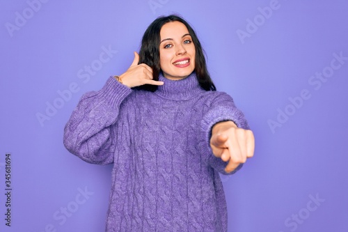 Young beautiful woman wearing casual turtleneck sweater standing over purple background smiling doing talking on the telephone gesture and pointing to you. Call me. © Krakenimages.com