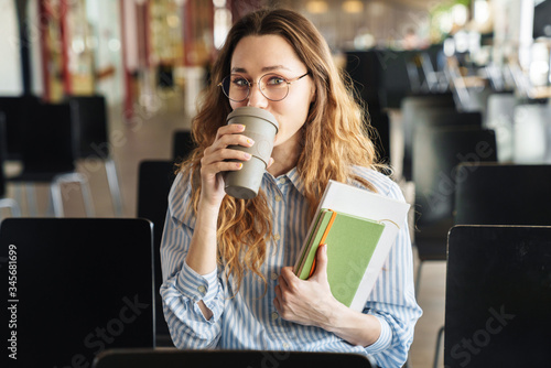Image of young woman drinking coffee takeaway and holding exercise books