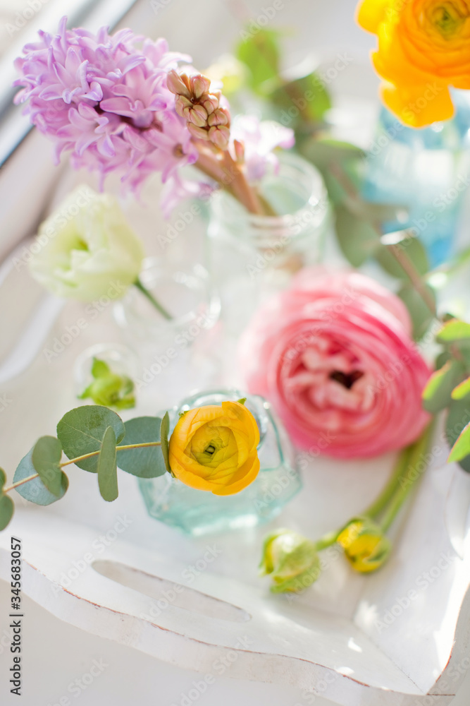 Beautiful colorful flowers in a glass bottles on a vintage wooden tray.