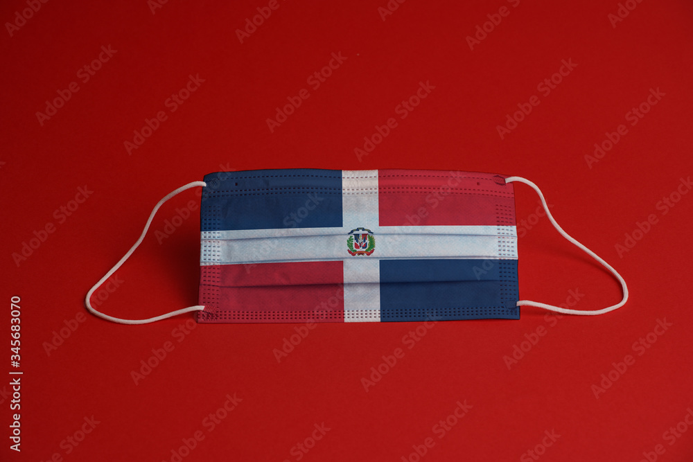 Obraz premium Coronavirus protective mask. Medical mask combined with the Dominican Republic flag. Red background. Face mask protection against pollution, virus, flu. Healthcare and surgery concept.