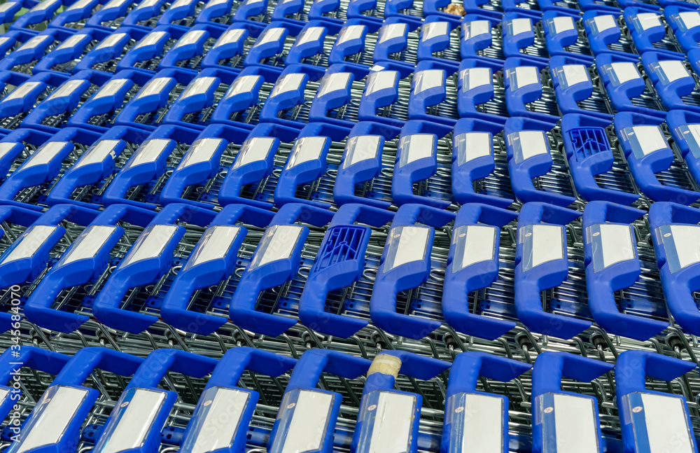 Parked shopping carts at the entrance to the supermarket. Metall carts with dark blue handles.