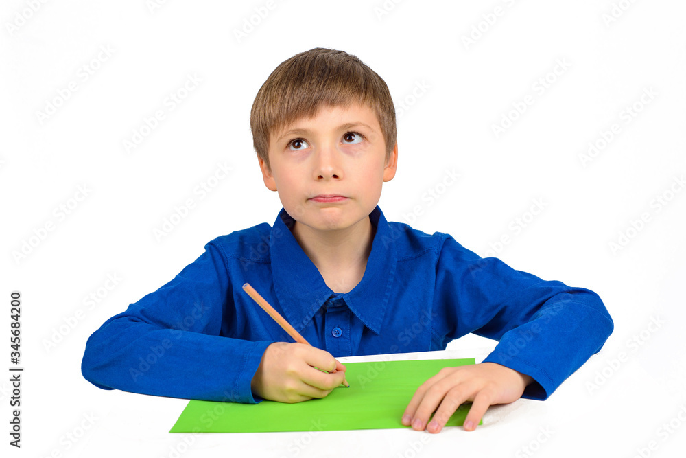 child development: a schoolboy boy in a blue T-shirt sits at the table and draws on colored paper child development: a schoolboy boy in a blue T-shirt sits at the table and draws on colored paper