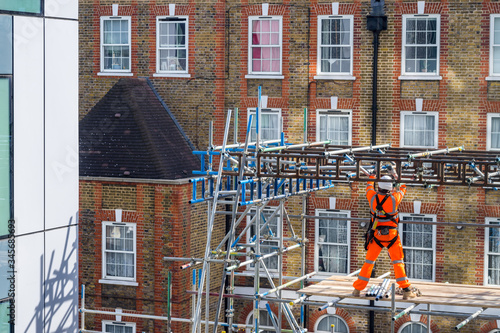 A scaffolder working on a building site, wearing orange hi-vis protection clothes. Concept for construction workers, building, work, infrastructure, building site, copy space, work and employment. photo