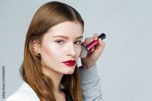 Make-up arstist applying cosmetinc powder on the face of fashion model. Beautiful healthy face of the young pretty woman with fresh skin.