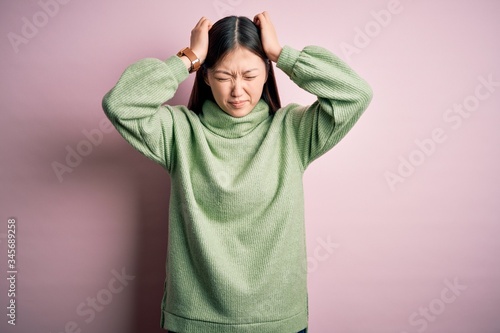 Young beautiful asian woman wearing green winter sweater over pink solated background suffering from headache desperate and stressed because pain and migraine. Hands on head. © Krakenimages.com