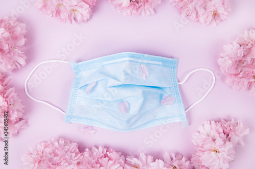 Medical protective mask and sakura flowers on a pink background.