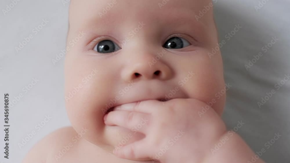 Close up face with soft tender skin of cute child lying on bed chewing fingers Close up face with soft tender skin of cute child lying on bed chewing fingers