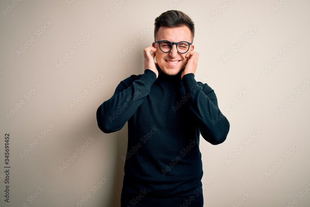 Young handsome caucasian man wearing glasses and casual sweater over isolated background covering ears with fingers with annoyed expression for the noise of loud music. Deaf concept. Young handsome caucasian man wearing glasses and casual sweater over isolated background covering ears with fingers with annoyed expression for the noise of loud music. Deaf concept.