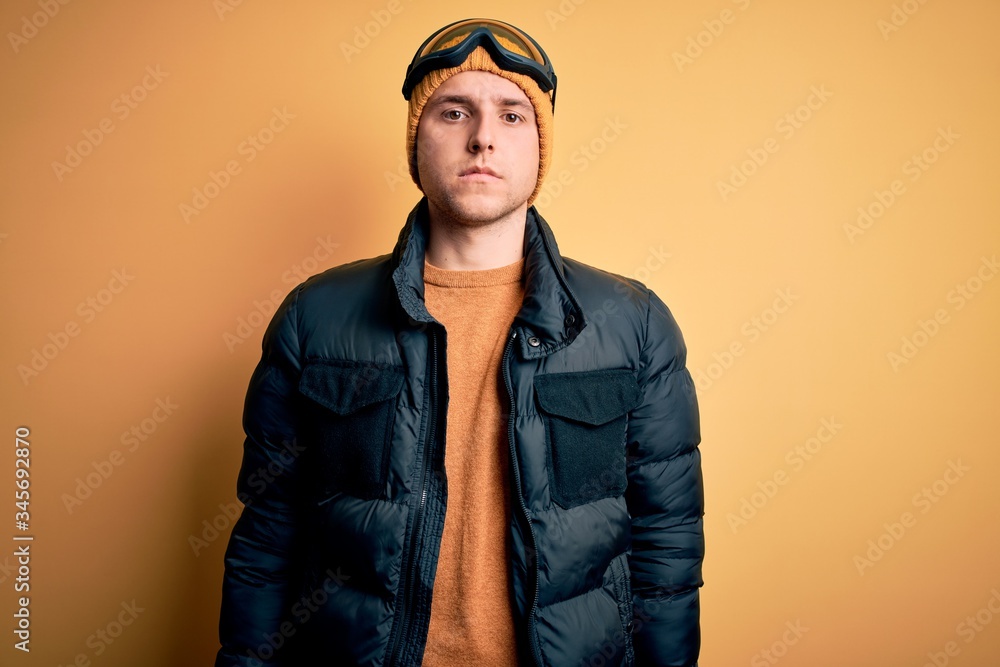 Young handsome caucasian man wearing hat, coat and ski glasses for winter and snow weather Relaxed with serious expression on face. Simple and natural looking at the camera. Young handsome caucasian man wearing hat, coat and ski glasses for winter and snow weather Relaxed with serious expression on face. Simple and natural looking at the camera.