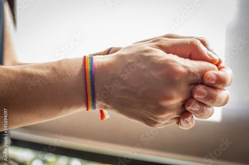 Different postures of hands with a bracelet with the flag GAY-LGTB on a yellow and white background.n