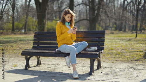 Young girl with headphones using phone in a city park.