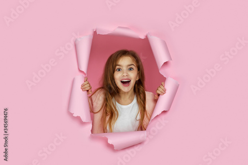 Canvas Print Portrait of cute surprised caucasian little child girl looking with happy face expression at the camera in torn paper pink wall