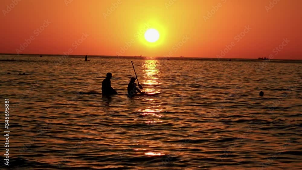 A scene of people at sea bathing and rowing during beautiful sunset at the end of hot winter day at beach in Phuket, Thailand. A scene of people at sea bathing and rowing during beautiful sunset at the end of hot winter day at beach in Phuket, Thailand.
