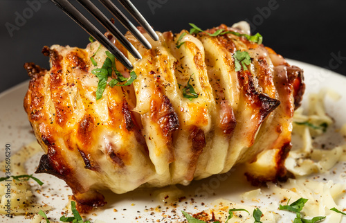 Accordion potatoes filled with bacon, sausages and cheese with herbs on the plate