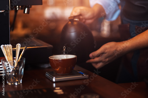 barista pouring boiling water from kettle to drip coffee maker.