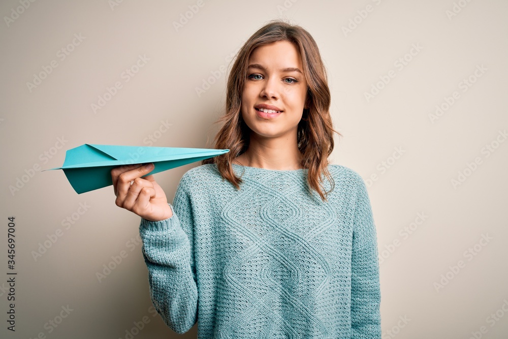 Young blonde girl holding paper plane as success on business and communication with a happy face standing and smiling with a confident smile showing teeth Young blonde girl holding paper plane as success on business and communication with a happy face standing and smiling with a confident smile showing teeth