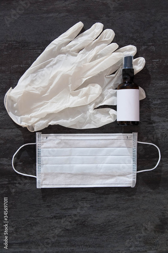 Disposable medical mask, rubber gloves and antiseptic in a bottle with grey background, top view.